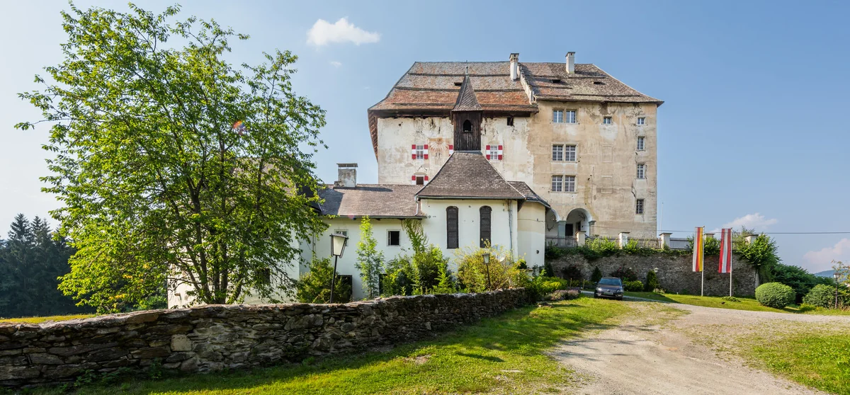 Schloss Moosburg hinter einer alten Steinmauer, umgeben von Bäumen und Wiesen